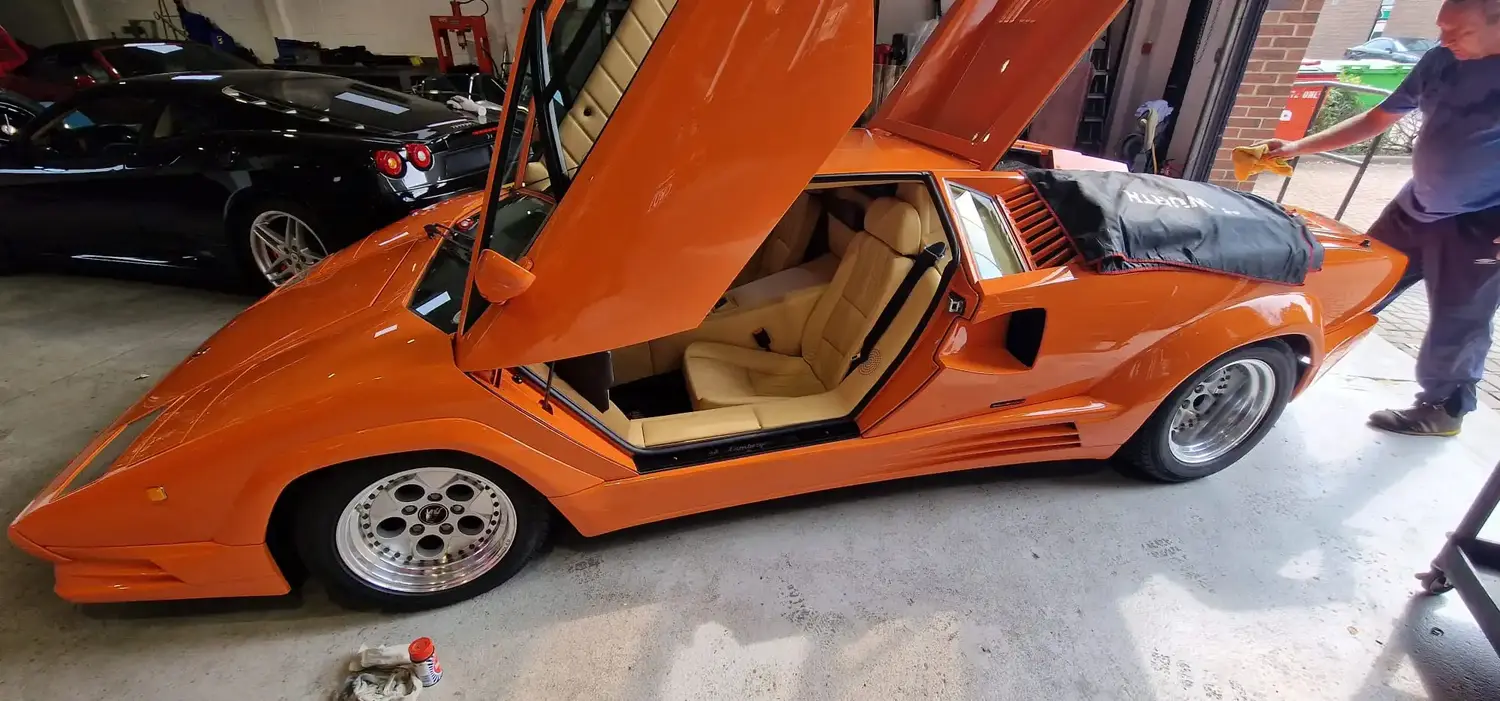 Side shot of a classic bright orange Lamborghini, with the owner polishing it