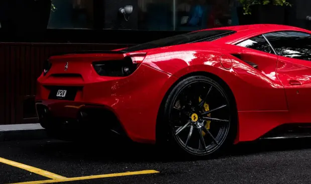 Side shot of a bright red Ferrari car parked along side the curb.